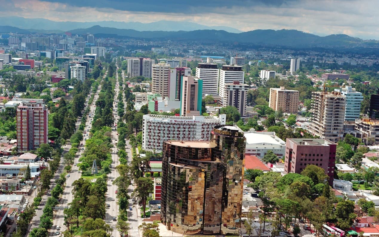La Avenida La Reforma vista desde el aire: el bulevar arbolado que cruza la Ciudad de Guatemala, con la sierra cerrando el fondo.